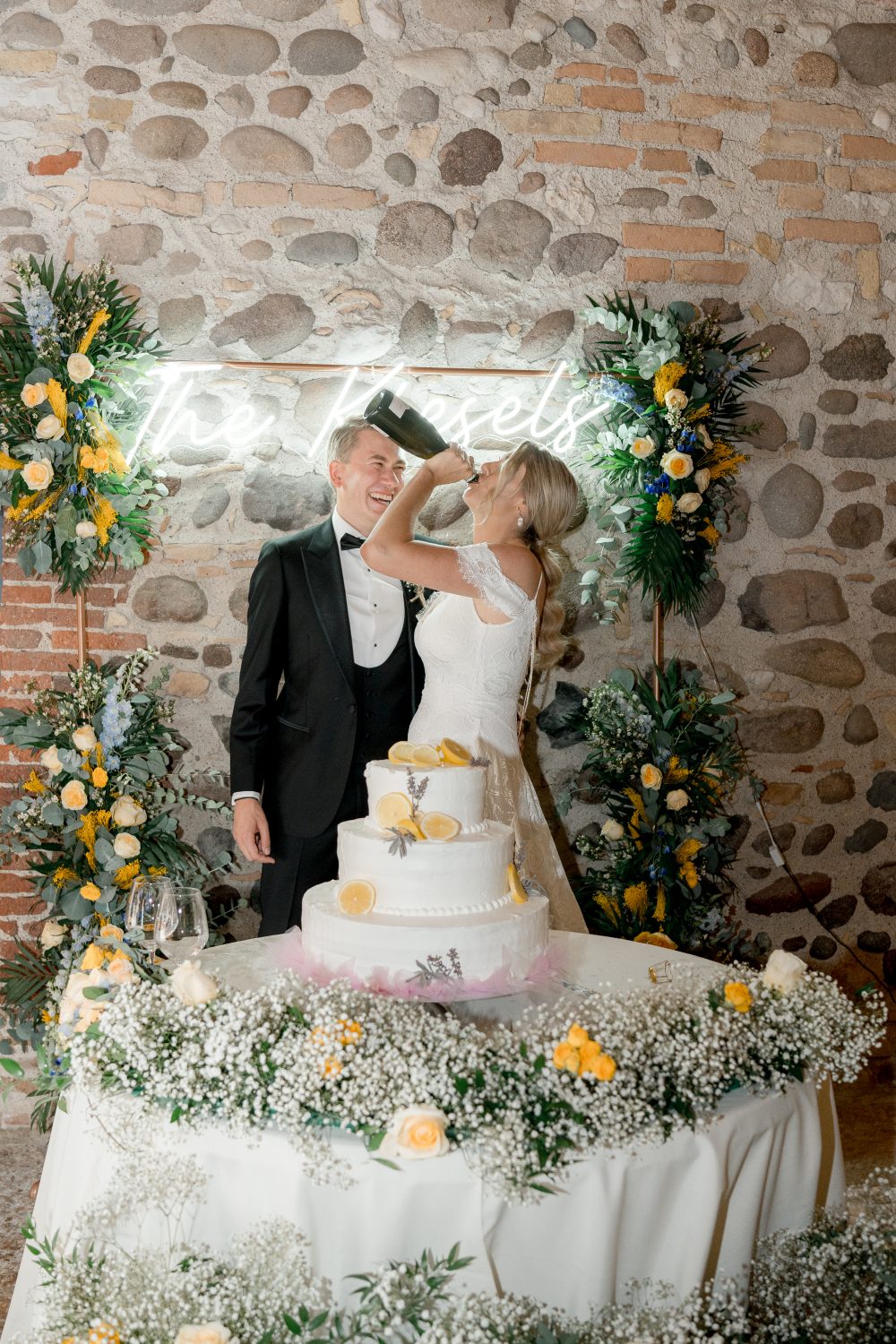 Sposi davanti alla torta nuziale con decorazioni di limoni e fiori, matrimonio in stile mediterraneo con sfondo in pietra